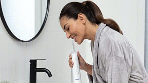 Woman standing over the bathroom sink using a water flosser