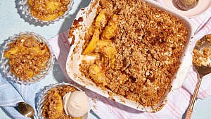 Peach crisp in a pink square baking tray with peach crisp served in three glass bowls around it.