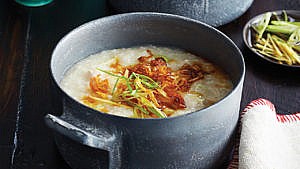 rice congee served in a grey ceramic bowl garnished with scallions and crispy fried shallots.