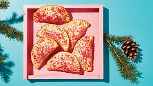 Sugar-dusted mincemeat turnovers in a pink box beside pine needles and a pine cone