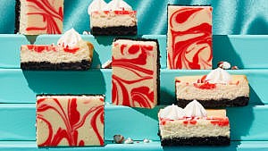 White and red marbled peppermint bark cheesecake bars arranged on cascading blue steps