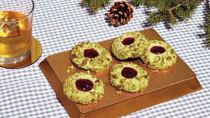 Five pistachio thumbprint cookies arranged on a golding serving mat.