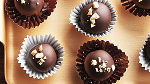peanut butter balls with chocolate coating sprinkled with chopped peanuts in a gold or silver foil cup on a gold tray