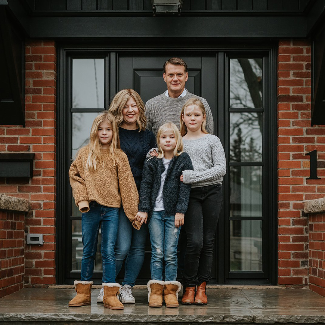 Sherry Wilcox, a breast cancer survivor, with her family—three children and husband—pose in front of a red-bricked house.