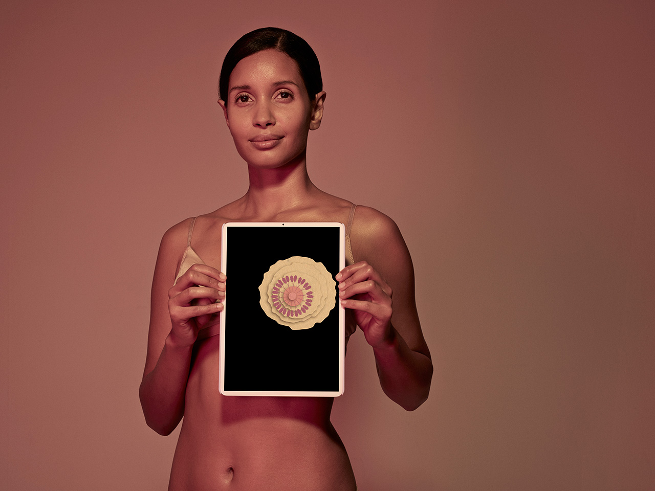 A woman holds a black tablet with an illustration of a breast over it, representing people being diagnosed with breast cancer at younger ages