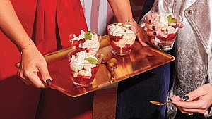 A person offering a tray of Cranberry and Clementine Eton Mess to a happy party guest
