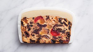A piece of marzipan frosted decadent fruitcake on a marble surface.