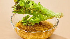 A lettuce leaf set atop a small bowl of dijon-mustard vinaigrette