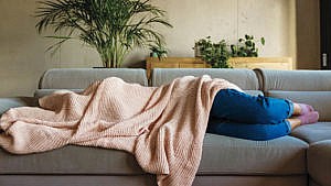 A person lying on a couch with a blanket over their head, representing a hangover