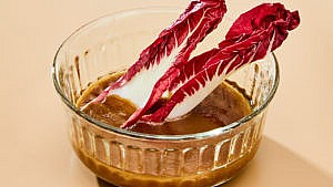 Two radicchio leaves dipped in a small bowl of honey-balsamic vinaigrette
