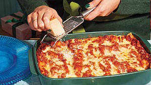 Cheese being grated over a tray of Nonna Maria's Lasagna Bolognese.
