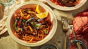 Two bowls of Romesco mussel linguine served on a tablecloth-covered surface