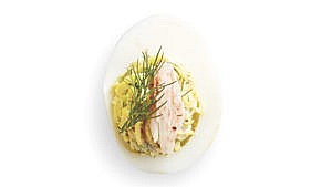 Crab-filled devilled eggs with dill in a small white bowl.